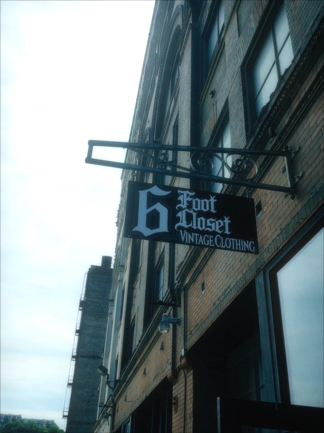 The 6 Foot Closet hanging sign, blackletter lettering reading 6 Foot Closet Vintage Clothing, on a red brick warehouse in the West Bottoms