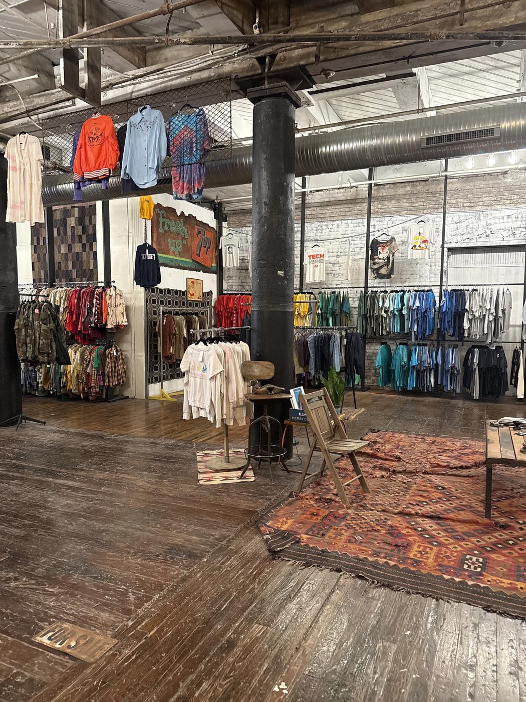 Inside 6 Foot Closet: color sorted racks under exposed ductwork and a cast iron column, with rugs on a worn wood floor