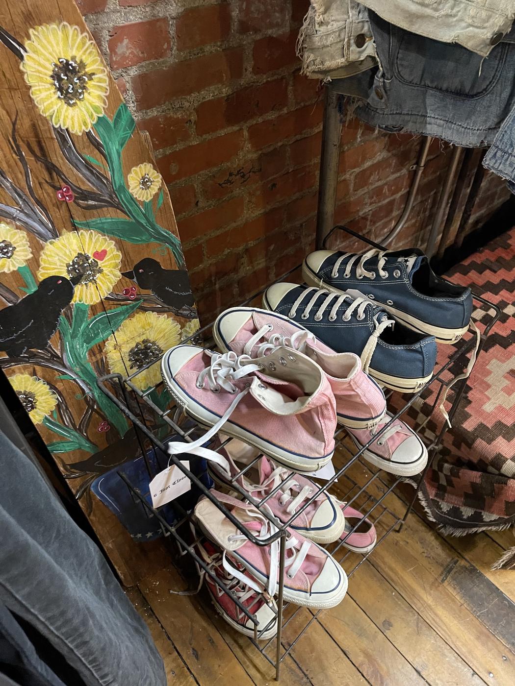 Pink and navy canvas sneakers on a wire rack beside a hand painted folk art board