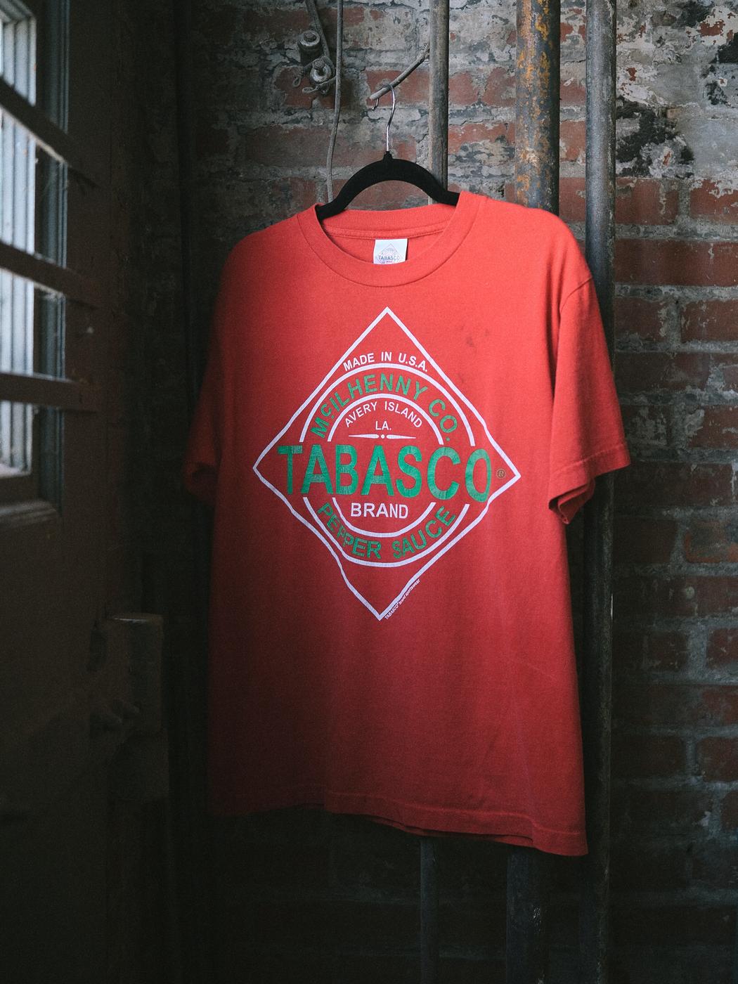 A faded red Tabasco brand tee shirt on a hanger in a window frame