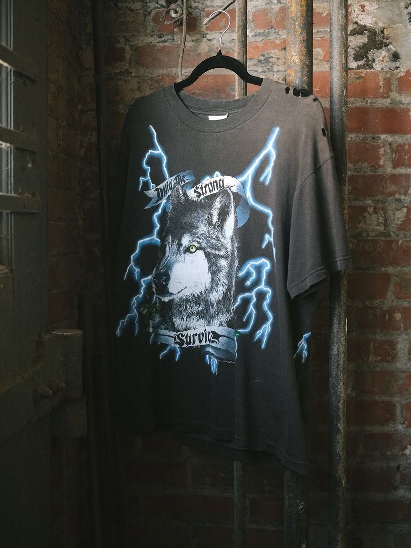 A vintage Only the Strong Survive tee shirt on a hanger against the painted brick wall at 6 Foot Closet